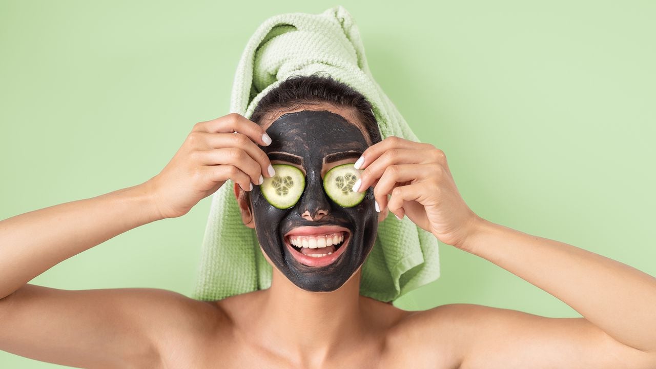 Happy smiling girl applying facial carbon mask portrait - Young woman having skin care cleanser spa day - Healthy beauty clean treatment and and self care lifestyle concept - Green background