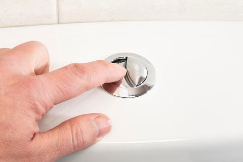 Mans' hand pushing the flush button on a toilet.
