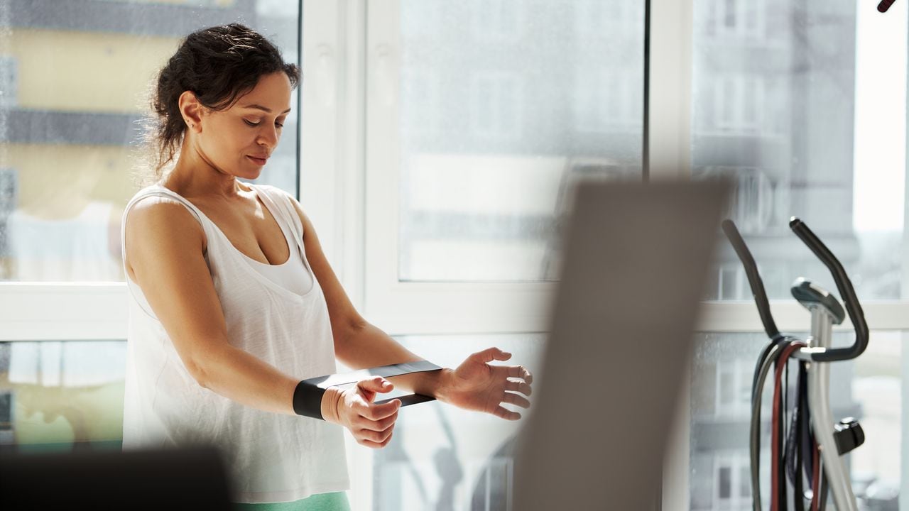 Retrato lateral de una mujer joven haciendo ejercicio con banda elástica de goma en casa. Entrenamiento, estiramiento, fitness en casa.
