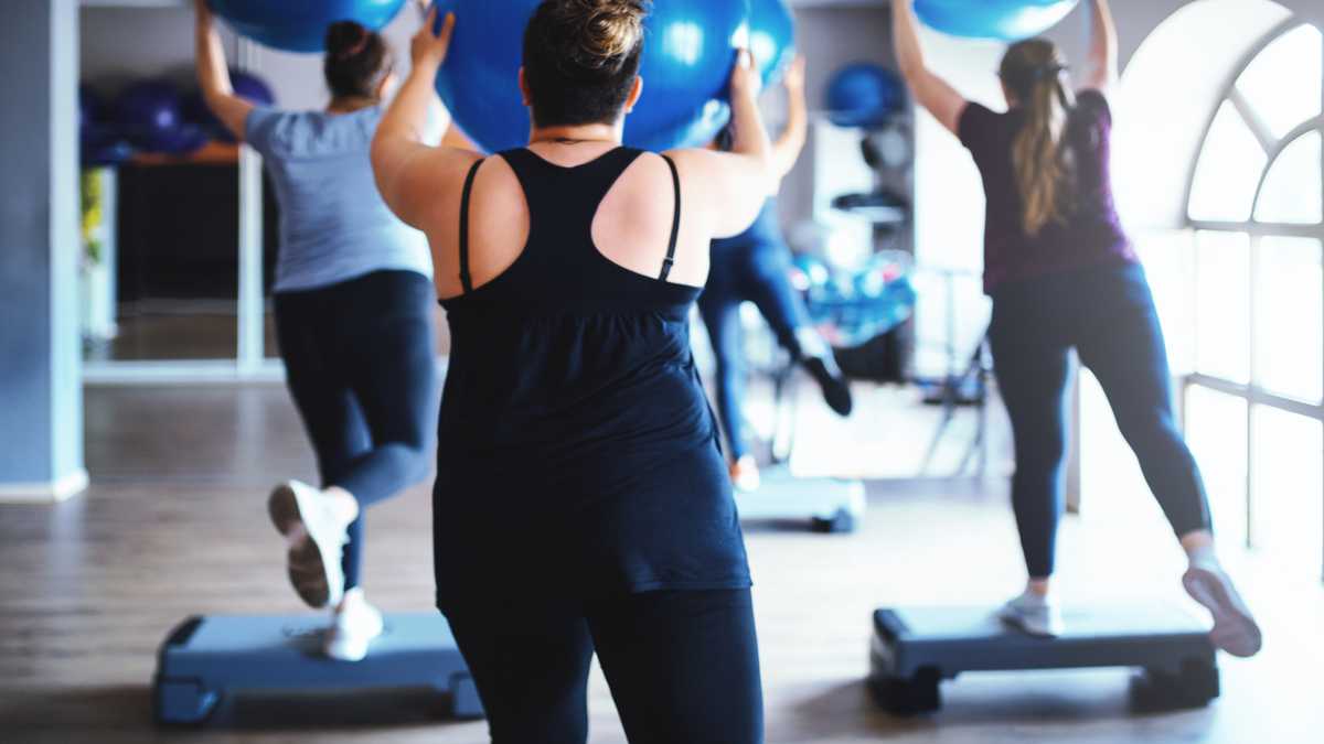 Rear view of overweight women working out together with a fitness ball and step platforms in the gym.