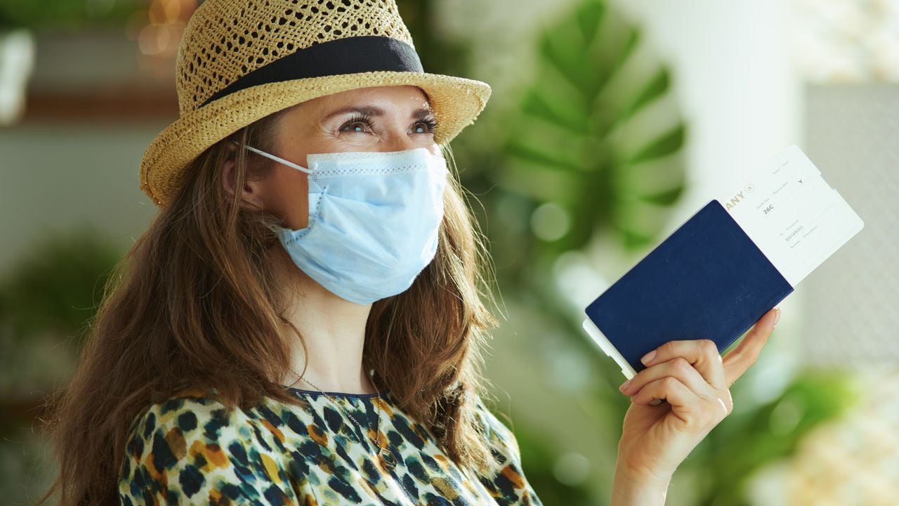 La vida durante la pandemia del covid-19. mujer de moda soñadora con sombrero de paja con máscara médica, pasaporte y boleto aéreo mirando en la distancia.