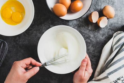 Whipping white eggs with whisk, in a palte. Top view of woman's hands mixing eggs.