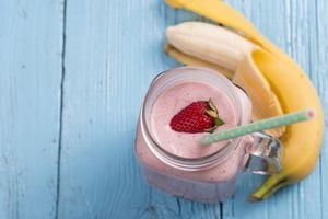 Fresh organic strawberry smoothie with banana on blue wooden background