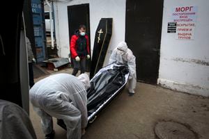 Medical workers in protective suits move a coffin with the body of a COVID-19 victim at the morgue of Infectious Hospital No. 5 in Nizhny Novgorod, Russia, on Wednesday, Oct. 20, 2021. The low vaccination rate in Russia, where only about a third of the population is fully vaccinated, is causing concern as the country suffers a sharp rise in cases, setting records for infections and deaths nearly every day this month. ​(AP Photo/Roman Yarovitcyn)