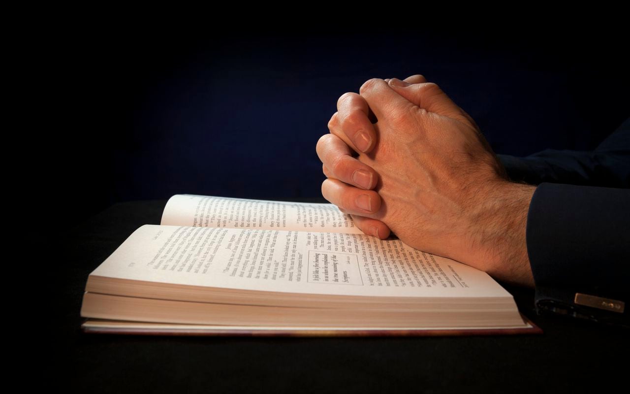 Clasped hands on a bible while praying to God.