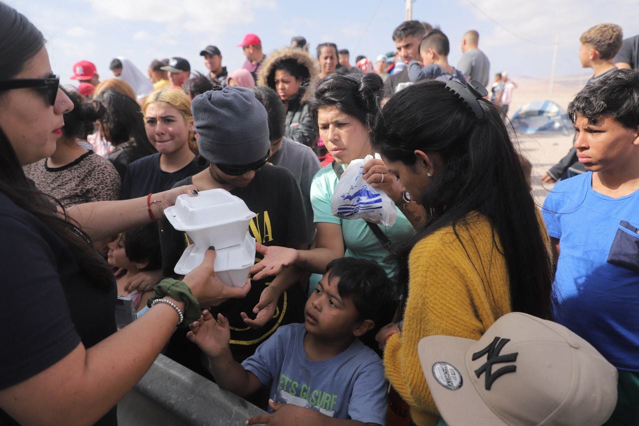 Migrantes venezolanos reciben alimentos mientras esperan información para ingresar a Perú en Arica, en la frontera entre Chile y Perú. (Foto de AGUSTÍN MERCADO / AFP)