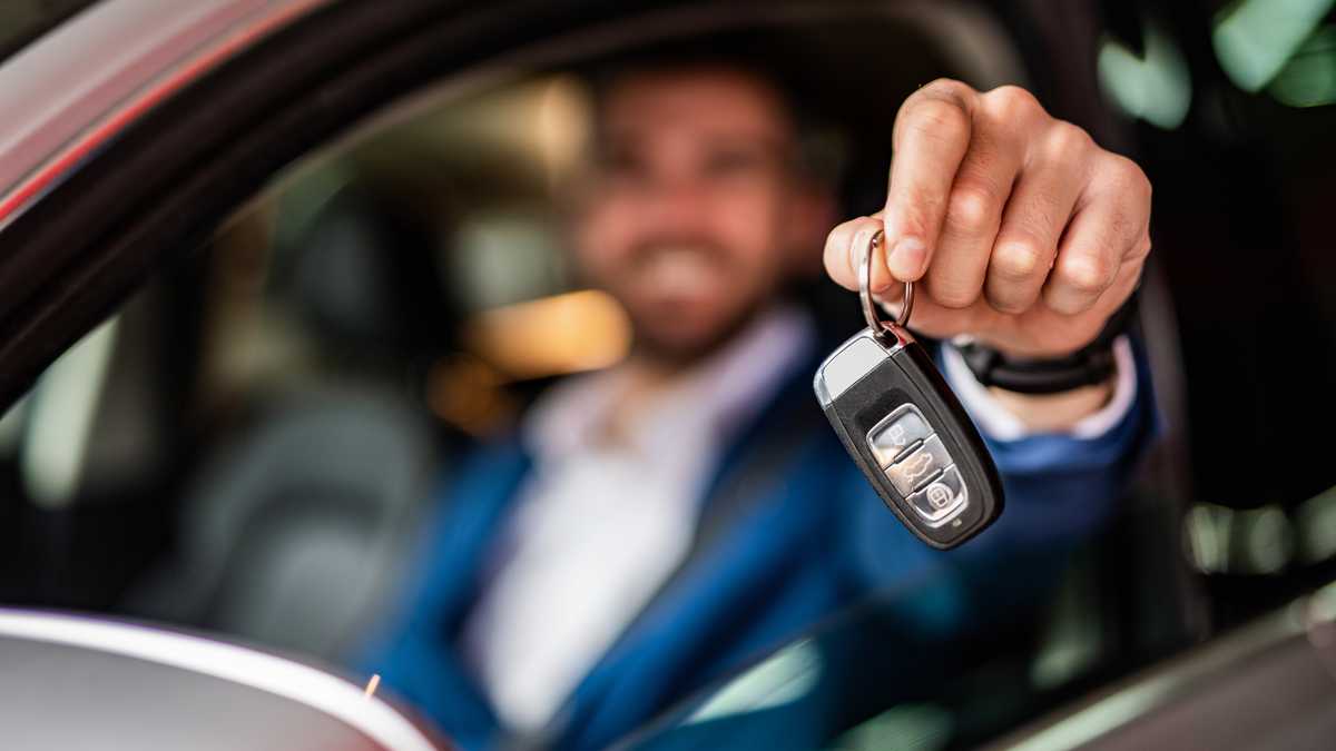 Photo of mid adult man sitting in new car and showing car keys. Focus on foreground.