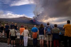 Los turistas miran y toman fotos de un volcán mientras continúa en erupción en la isla canaria de La Palma, España, el martes 26 de octubre de 2021. (AP Photo/Emilio Morenatti)
