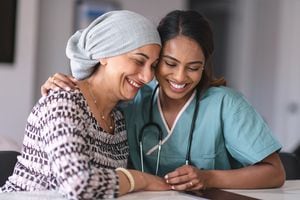Retrato de una mujer india que lucha contra el cáncer con su médico. El doctor es una mujer mixta. Las dos mujeres están sentadas junto a la otra en el interior. Están abrazando y riendo.