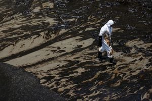 Un trabajador camina tras un derrame de petróleo causado por olas anormales, provocadas por una erupción volcánica submarina masiva a medio mundo de distancia en Tonga, en la playa peruana de Ventanilla, Perú, 18 de enero de 2022. Foto REUTERS/Pilar Olivares