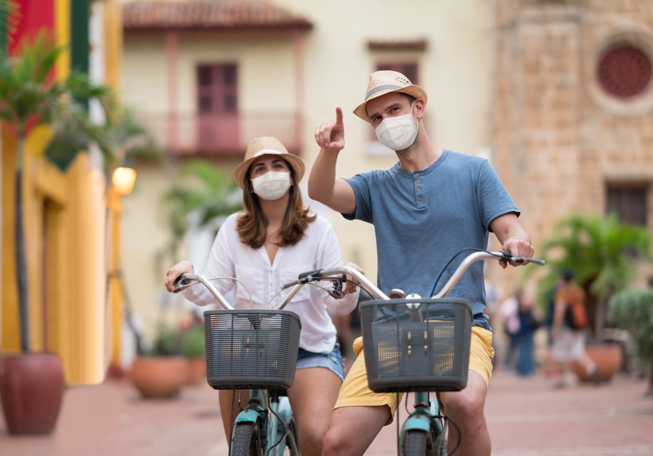 Pareja feliz haciendo turismo en bicicleta en Cartagena con mascarilla para evitar la pandemia de COVID-19: conceptos de estilo de vida