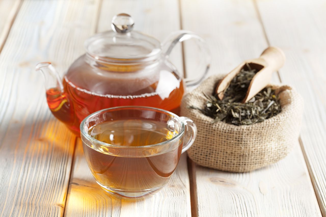 Taza de té, tetera y hojas de té en la mesa de madera