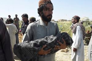 A man carries the body of his child, who was killed after a roof of a house collapsed, as he arrives for a burial following an earthquake in the remote mountainous district of Harnai on October 7, 2021, as around 20 people were killed and more than 200 injured when a shallow earthquake hit southwestern Pakistan in the early hours of October 7. (Photo by Banaras KHAN / AFP)