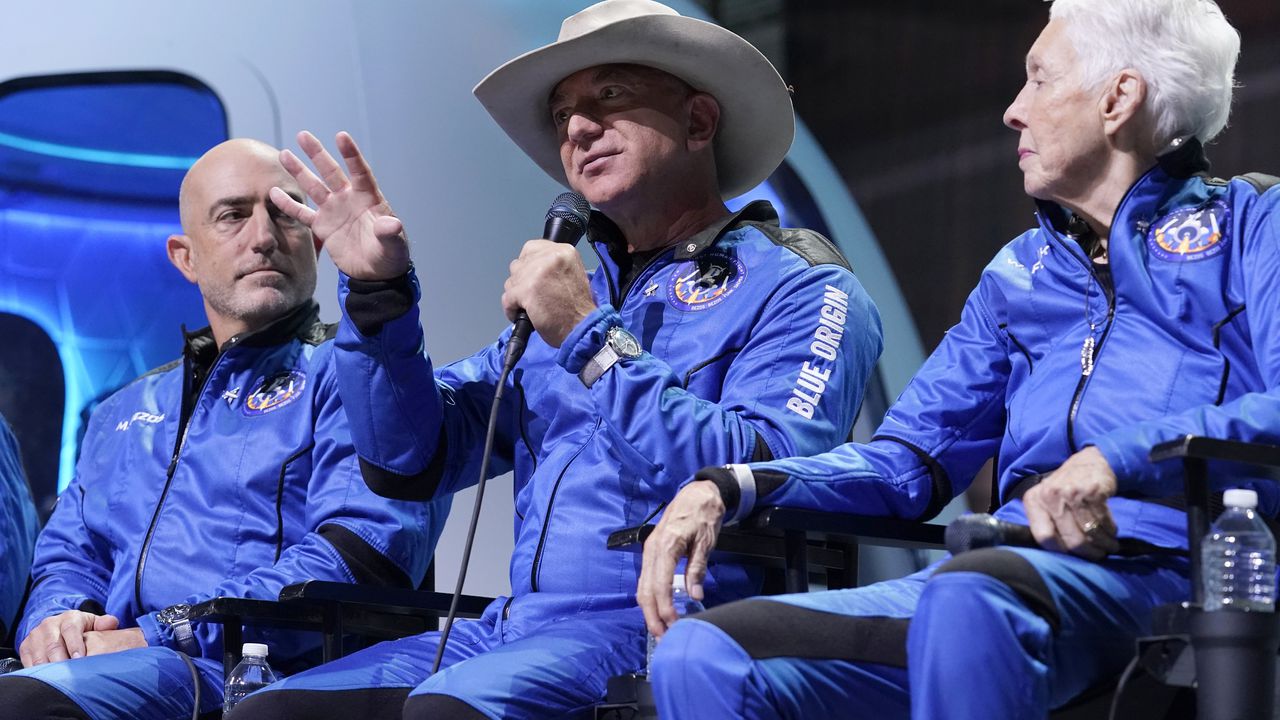 Mark Bezos, left, and Wally Funk, right, listen as Jeff Bezos, center, founder of Amazon and space tourism company Blue Origin makes comments about their flight experience during a post launch briefing at its spaceport near Van Horn, Texas, Tuesday, July 20, 2021. (AP Photo/Tony Gutierrez)