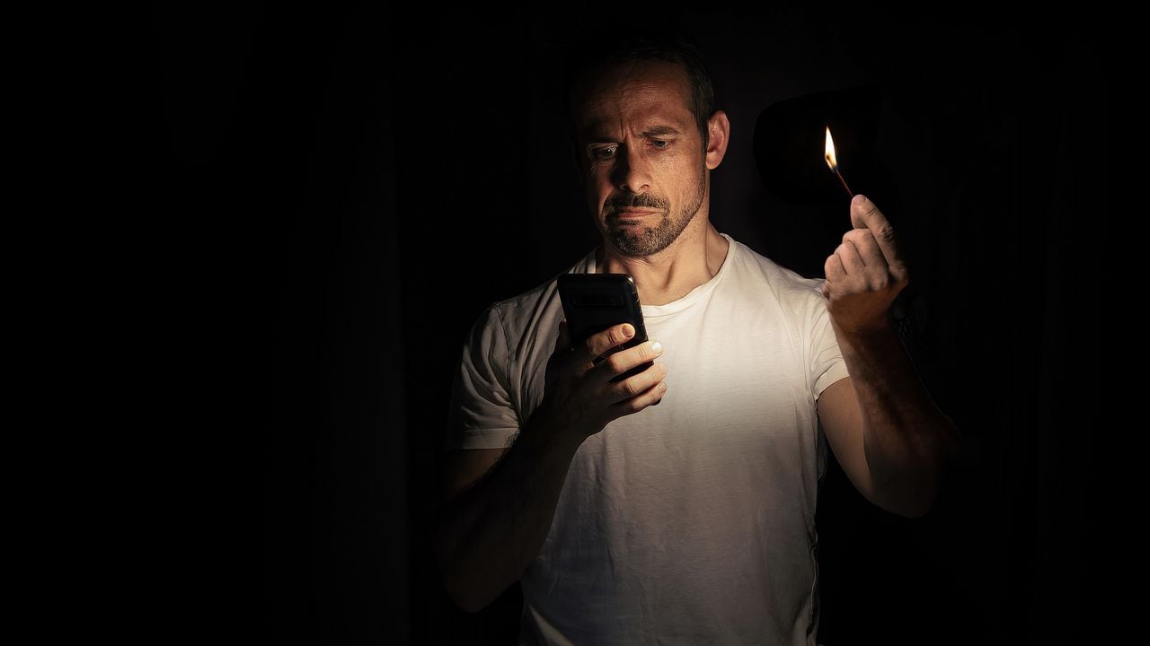 Hombre mira que su teléfono no tiene batería, mientras no hay luz en su casa.