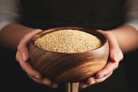 Woman holding wooden bowl with white quinoa on dark background, closeup