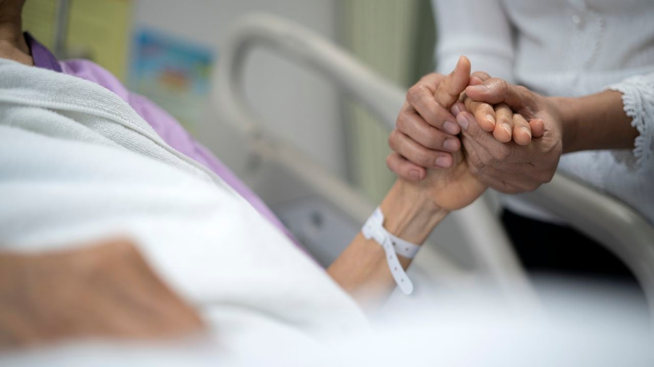 Foto de una hija sosteniendo la mano de su madre en la cama de un hospital