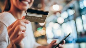 Retrato de mujer joven haciendo compras en línea con smartphone y pago con tarjeta de crédito. Mujer sosteniendo teléfono inteligente y tarjeta de crédito en un café urbano. El foco está en la tarjeta.