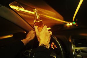 El conductor del automóvil sostiene una bebida alcohólica mientras conduce de noche