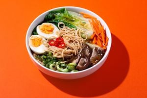 Ramen noodle soup with eggs, mushrooms, pak choi in white bowl on bright orange background with shadow, top view, copy space