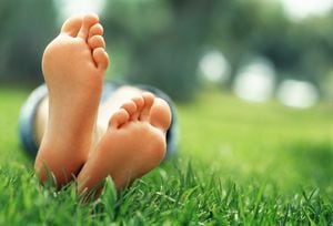 Close-up of an 18 year old woman with crossed feet lying in grass, focus on feet, greenery out of focus in background, she is wearing a short blue skirt, empty space on right side, Morocco, Marrakech.