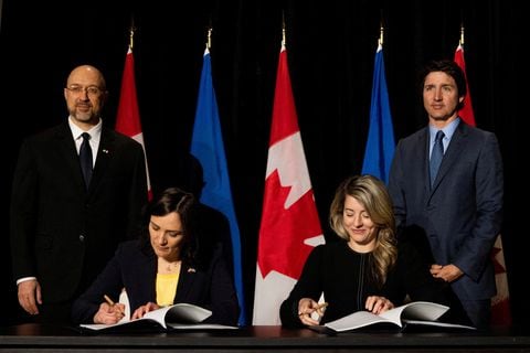 La embajadora de Ucrania en Canadá, Yuliya Kovaliv, firma un acuerdo con la ministra de Asuntos Exteriores de Canadá, Melanie Joly, mientras que el primer ministro de Ucrania, Denys Shmyha, y el primer ministro de Canadá, Justin Trudeau, observan en Toronto