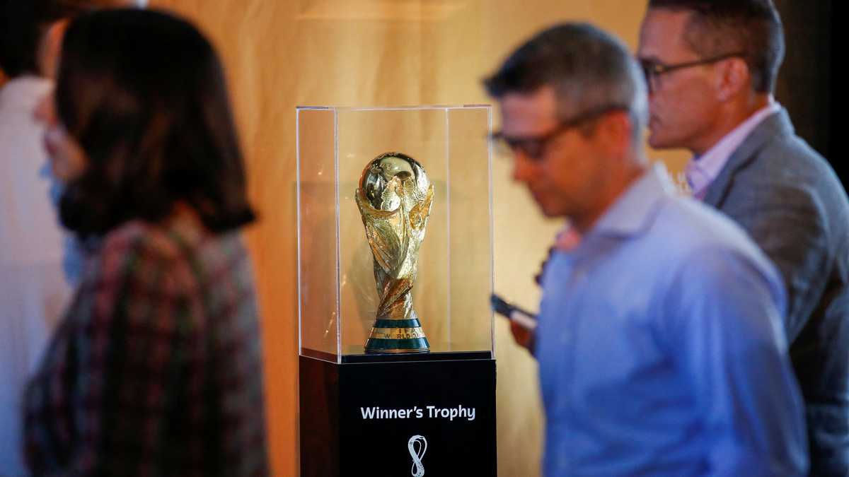 People walk next to the Official FIFA World Cup Trophy as it is displayed during the FIFA/Frito Lay news conference ahead of 2026 World Cup while in New York City, New York, U.S., June 17, 2022.  REUTERS/Eduardo Munoz