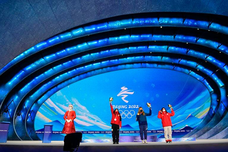 An hostess stands next to Silver medallist Spain's Queralt Castellet (L), gold medallist USA's Chloe Kim (C) and bronze medallist Japan's Sena Tomita (R) during the snowboard women's halfpipe victory ceremony of the Beijing 2022 Winter Olympic Games at the Zhangjiakou Medals Plaza in Zhangjiakou on February 10, 2022. (Photo by Tobias SCHWARZ / AFP)