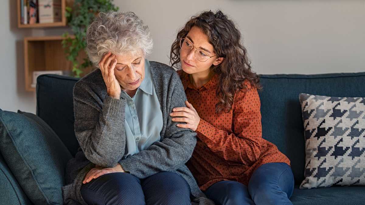 Caring daughter comforting frustrated unhappy senior woman. Loving adult granddaughter talking to sad depressed old grandmother holding hand and comforting her. Upset widowed woman with headache consoled by her daughter.