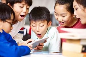 grupo de niños asiáticos de la escuela primaria que se reúnen alrededor de jugar juntos usando la tableta durante las vacaciones.