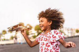Niño africano corriendo en la playa mientras juega con un avión de juguete de madera al atardecer, Concepto de estilo de vida juvenil y de viaje - Enfoque principal en el avión de mano