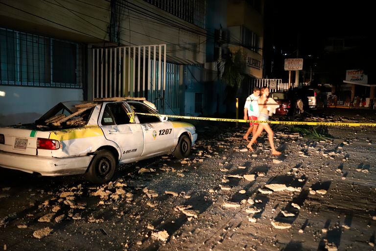 Una pareja pasa junto a un taxi que resultó dañado por la caída de escombros después de un fuerte terremoto en Acapulco, México, el martes, sept. 7 de febrero de 2021. (AP Photo/ Bernardino Hernandez)