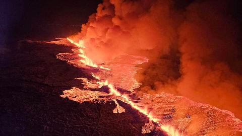 Ondas de humo y lava fluyendo que tiñen el cielo de color naranja durante una erupción volcánica.
