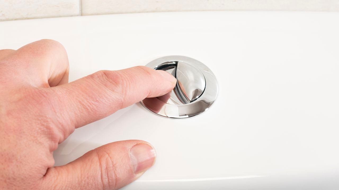 Mans' hand pushing the flush button on a toilet.