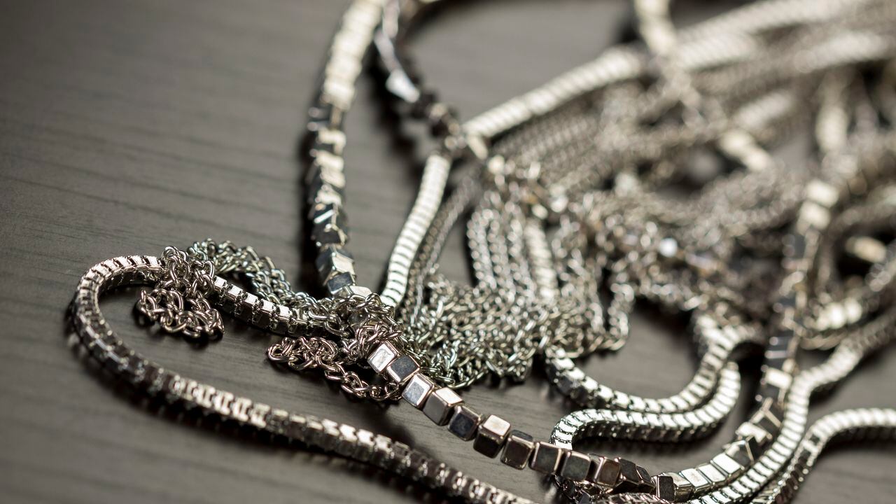 Assorted silver costume jewellery with a jumbled pile of chains with different shaped links, a clear crystal bead and a necklace of round silver beads with focus to the chains