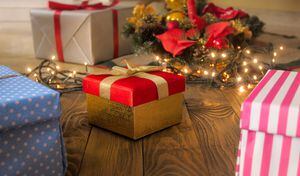 Hermosa caja de regalo roja con cinta dorada sobre piso de madera contra luces brillantes y árbol de Navidad. Fondo perfecto para las vacaciones