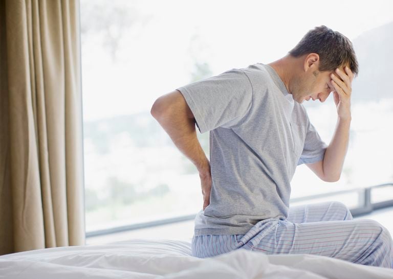 Hombre sentado en la cama con dolor de espalda y dolor de cabeza