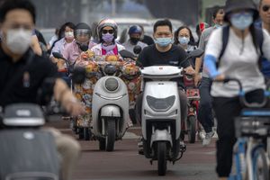 Los viajeros con mascarillas cruzan una intersección en el distrito comercial central de Beijing, el viernes 17 de junio de 2022. Foto AP/Mark Schiefelbein