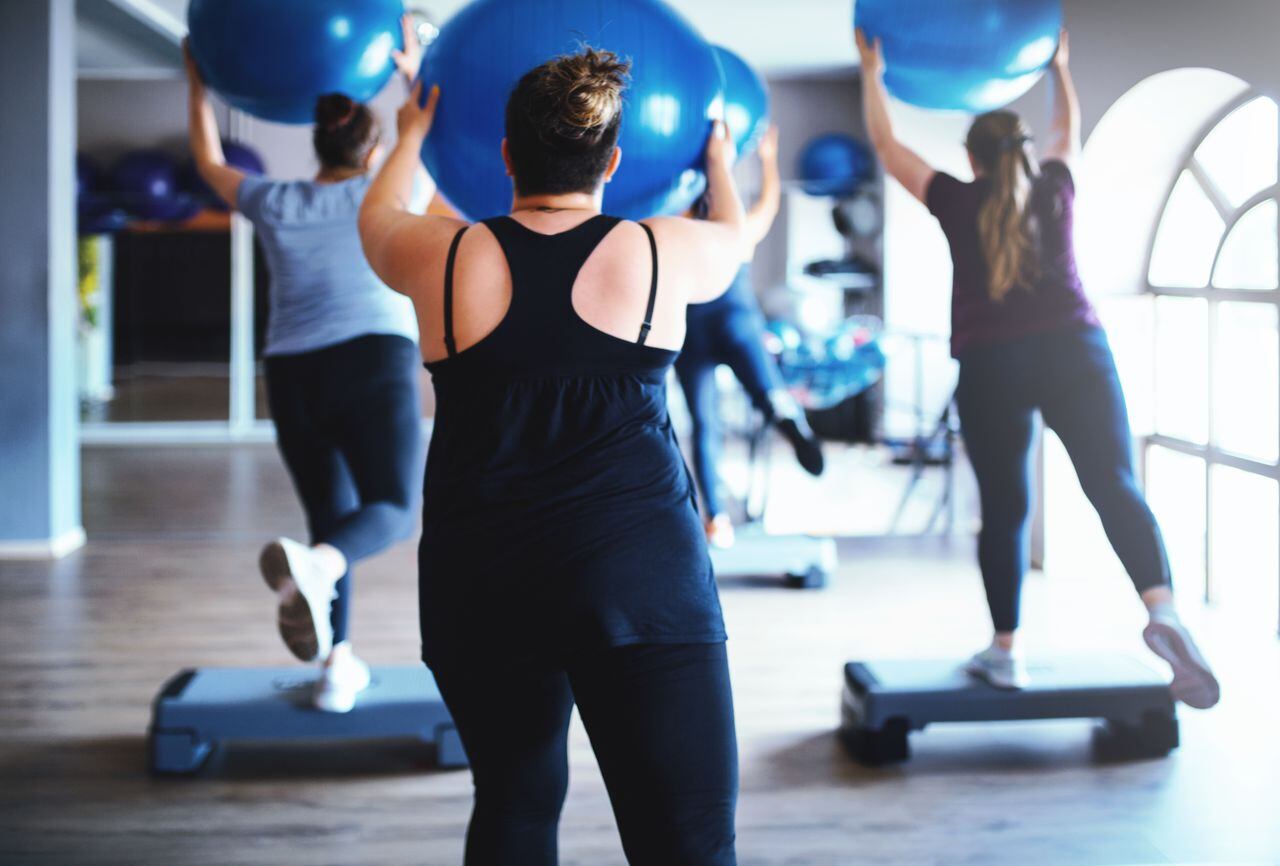 Rear view of overweight women working out together with a fitness ball and step platforms in the gym.