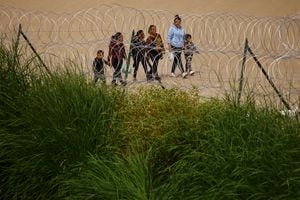 Migrantes pasan junto a una valla de alambre de púas desplegada para impedir el cruce de migrantes a Estados Unidos, vista desde Ciudad Juárez, México, el 28 de agosto de 2023.