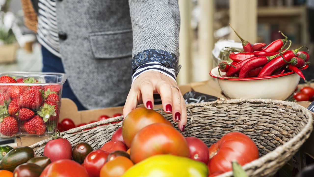 Close up of hand picking tomato from basket.