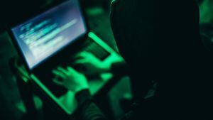 Hacker trabajando en la computadora por la noche bajo luz verde.