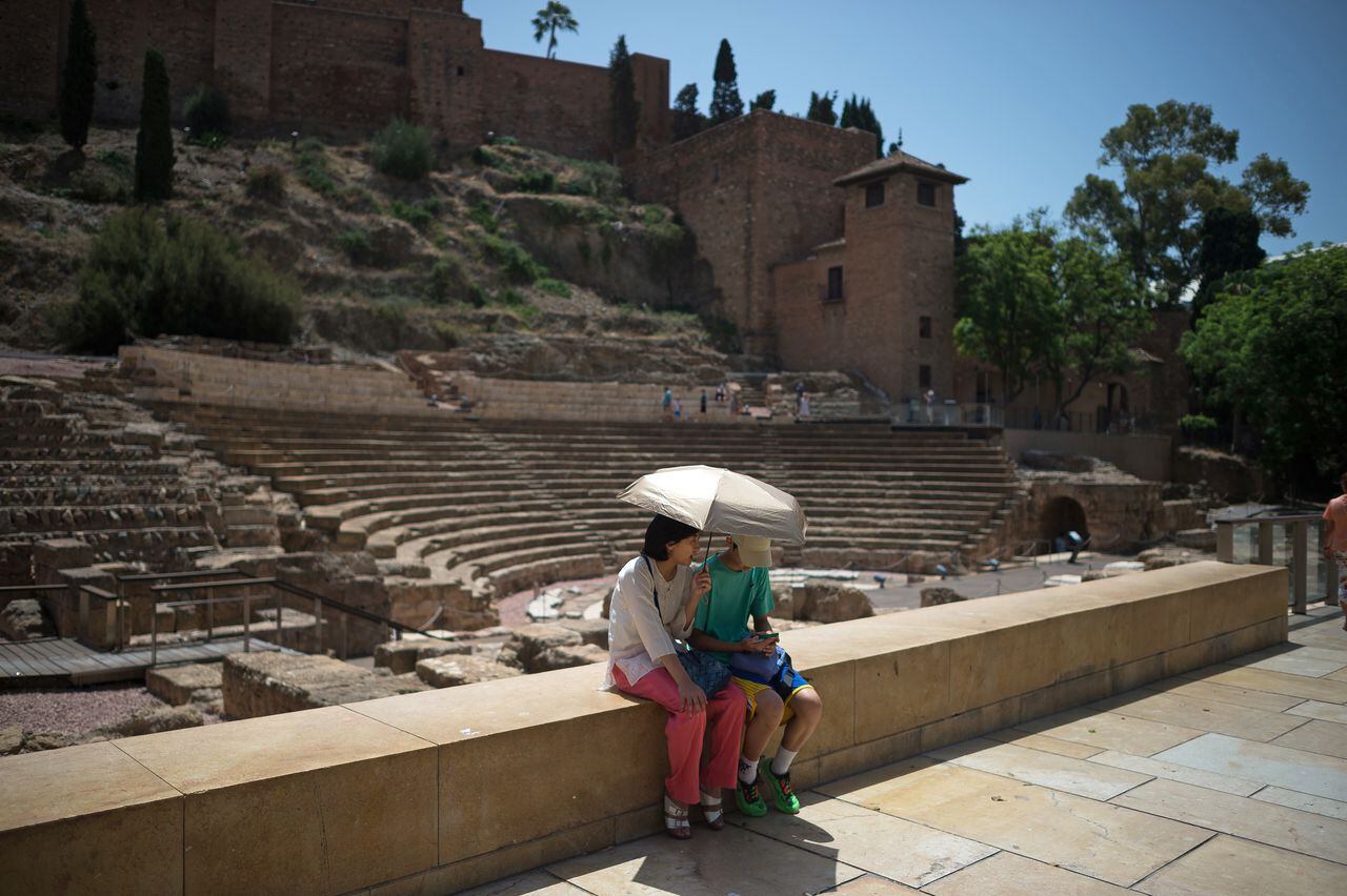 Se ve a los turistas sentados y sosteniendo un paraguas para protegerse del sol mientras descansan en el centro de la ciudad en medio de una intensa ola de calor en Málaga. España está experimentando altas temperaturas en todo el país.