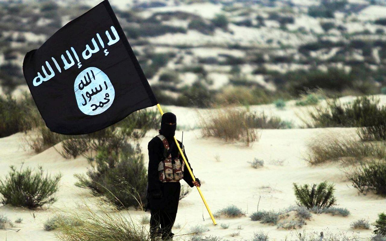 Un soldado enmascarado del Estado Islámico posa sosteniendo la pancarta de ISIL en algún lugar de los desiertos de Irak o Siria.