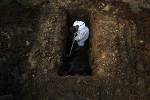 Un hombre con un traje de protección cava la tierra para enterrar el cuerpo de una persona que murió a causa de covid-19 en Gauhati, India