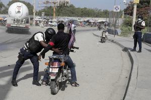 Un oficial de policía cachea a un motociclista en un puesto de control en Puerto Príncipe, Haití, el sábado 1 de julio de 2023.