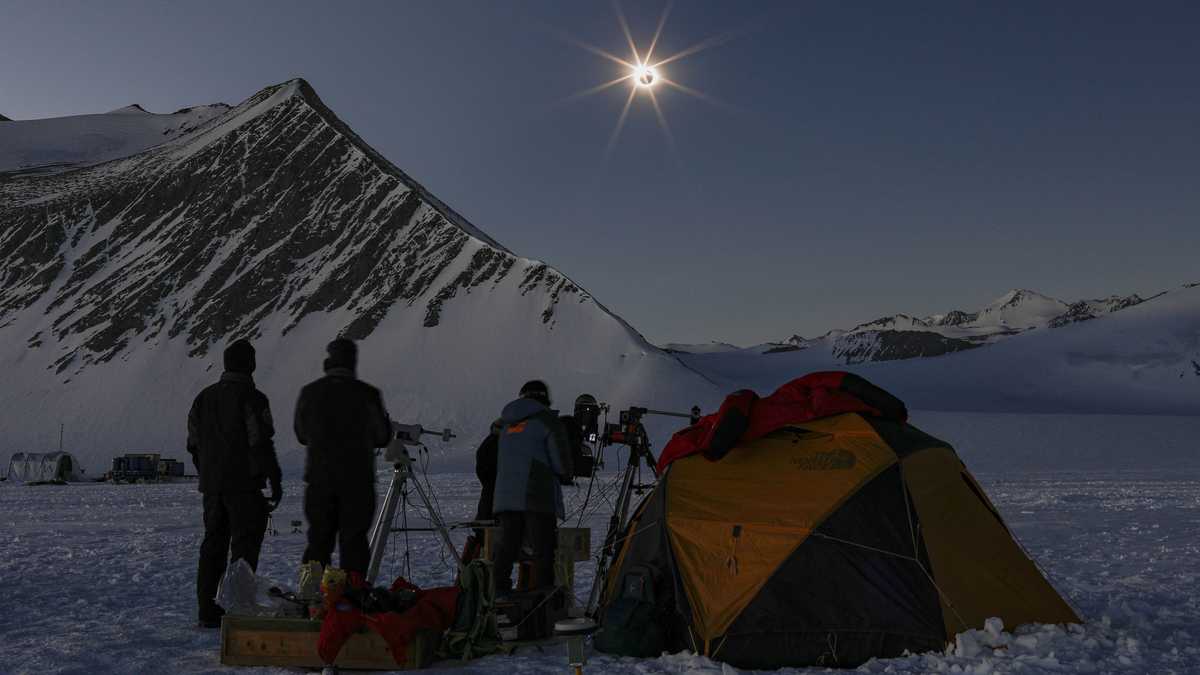 Científicos chilenos y estadounidenses mirando un eclipse solar desde el glaciar Unión en la Antártida el 4 de diciembre de 2021. (Foto por FELIPE TRUEBA / Imagen Chile / AFP)