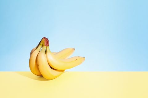Still life shot of bunch of five bananas on yellow table with blue background.