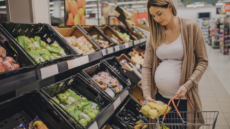A young pregnant woman is grocery shopping in a supermarket store.