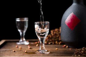 chinese liquor is pouring into a glass from a bottle on wood background